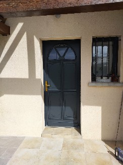 Pose d'une porte d'entrée en bois exotique gris extérieur et blanc intérieur.
